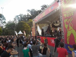 imagem mostra palco com decoração vermelha e público assistindo ao show