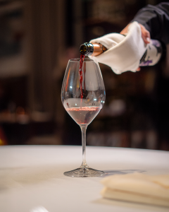 imagem mostra uma mão colocando vinho em uma taça de vidro