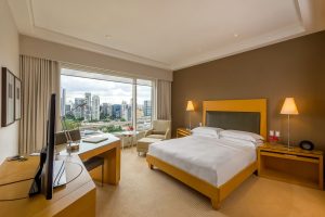 imagem mostra quarto de hotel com janela para a vista da cidade