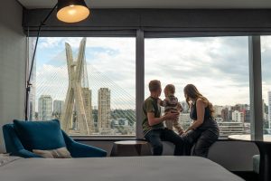 hiltonspmorumbi-quarto (1) imagem mostra casal com uma criança em um quarto de hotel apreciando a vista da cidade