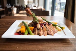 Prato gourmet com carne fatiada, legumes grelhados e molho, servido em restaurante.