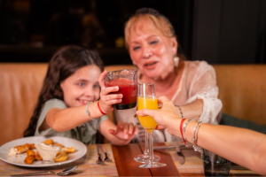 Mulher, criança e outra pessoa brindando bebidas durante brunch em restaurante