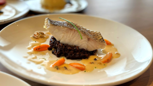 Prato de lombo de robalo servido com molho de vôngole e arroz negro.