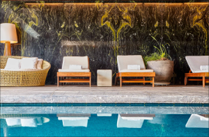 Ambiente interno do SPA by JW no JW Marriott Hotel São Paulo, com piscina de águas calmas, espreguiçadeiras estofadas, sofá de fibras naturais, vasos com plantas e parede de mármore escuro ao fundo.